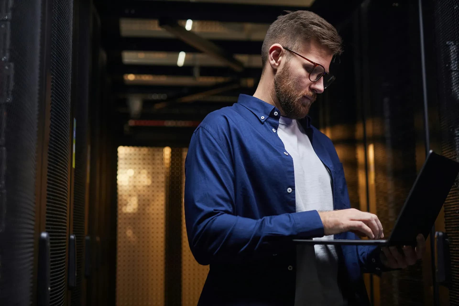 Tecnico con un laptop in mano fra gli armadi di una sala server